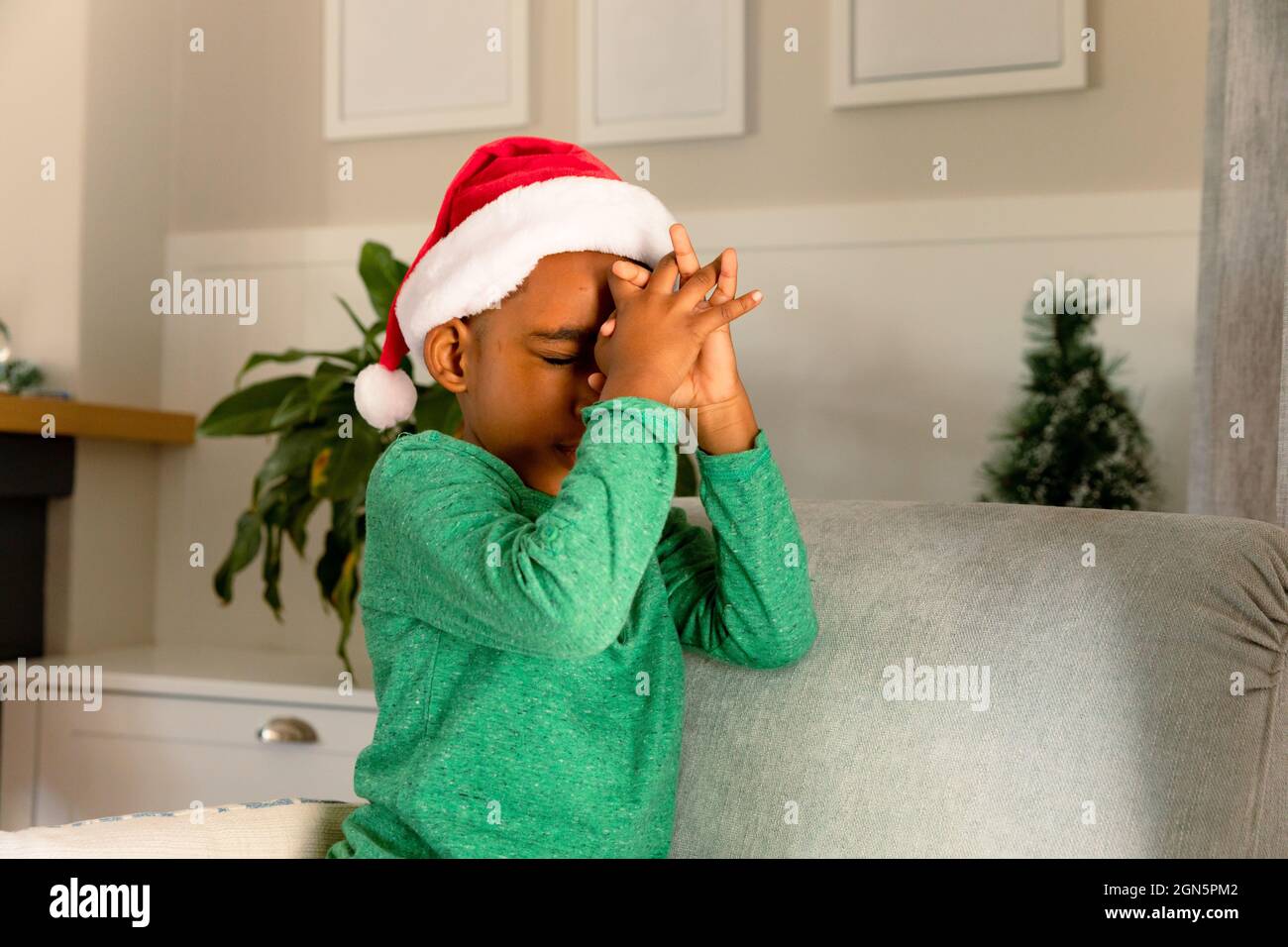 African american boy wearing santa hat and praying at christmas time Stock Photo
