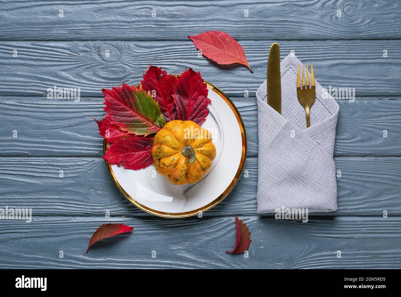 Beautiful table setting with pumpkin and autumn leaves on color wooden ...