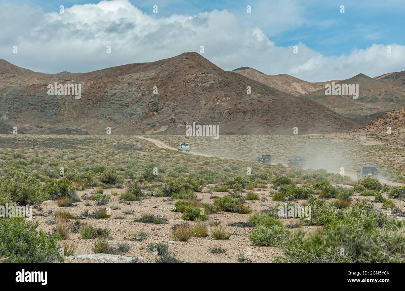 High Desert, Nevada, USA - May 17, 2011: I pickup truck and 3 SUVs drive on dirt road spewing dust in the air with mountain as backdrop under blue clo Stock Photo