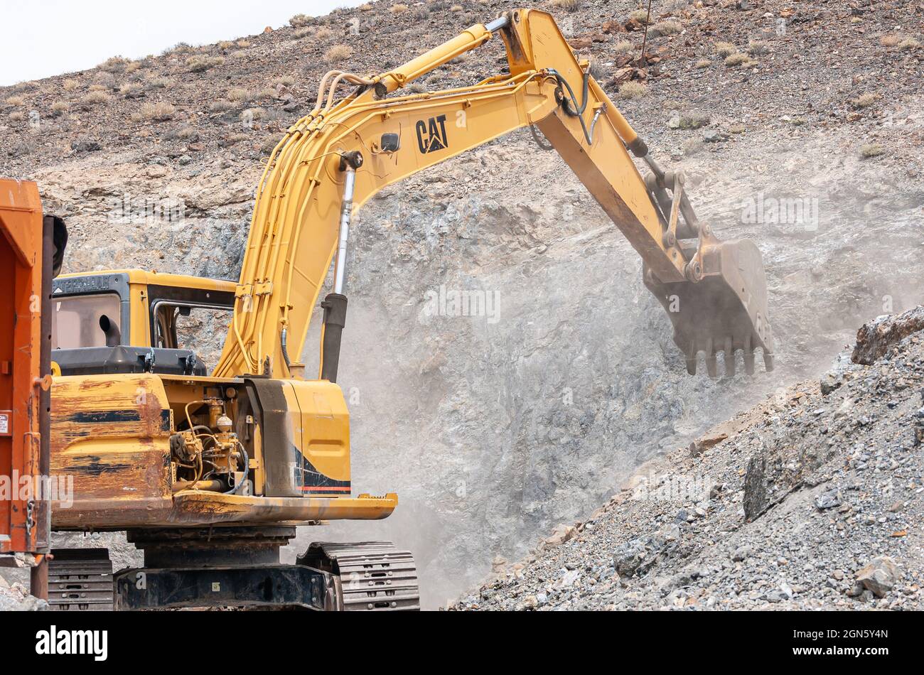 High Desert, Nevada, USA - May 17, 2011: Closeup of yellow CAT movable crane scrathing the gray flank of rocky hill throwing lots of dust in the air. Stock Photo