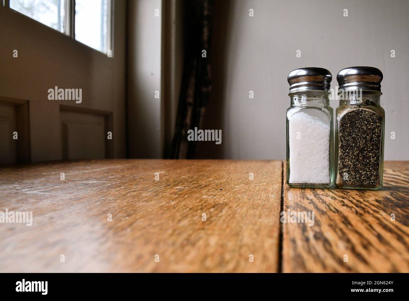 https://c8.alamy.com/comp/2GN624Y/ground-salt-and-pepper-shakers-on-a-polished-wood-surface-with-light-from-a-window-illuminating-the-table-rustic-dining-table-with-glass-shakers-2GN624Y.jpg