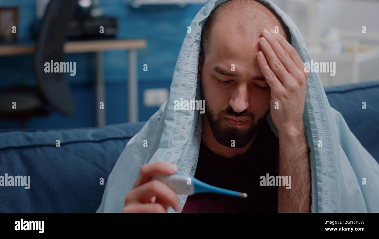 close-up-of-unwell-adult-looking-at-thermometer-and-measuring