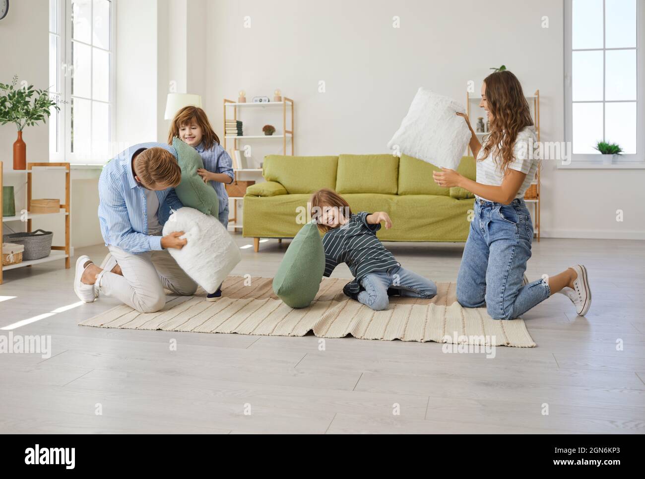 Happy young mother, father and children having a pillow fight in the living room Stock Photo