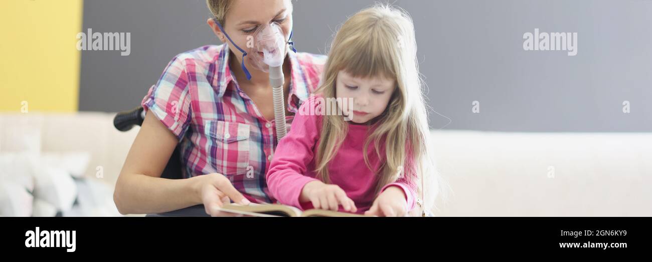 Woman in wheelchair and oxygen mask is reading book with little girl Stock Photo