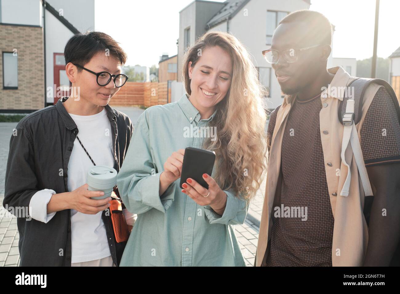 Horizontal medium portrait of three ethnically diverse friends hanging out together watching something in Internet on smartphone Stock Photo