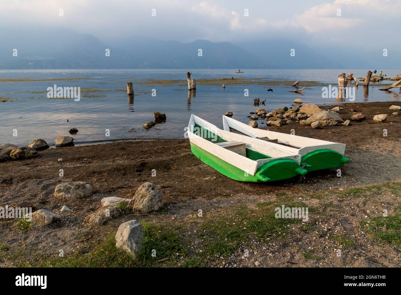 Two local fishermen canoes at the shore along lake Atitlan during sunset with view on misty volcanic mountains in San Pedro la Laguna, Guatemala Stock Photo