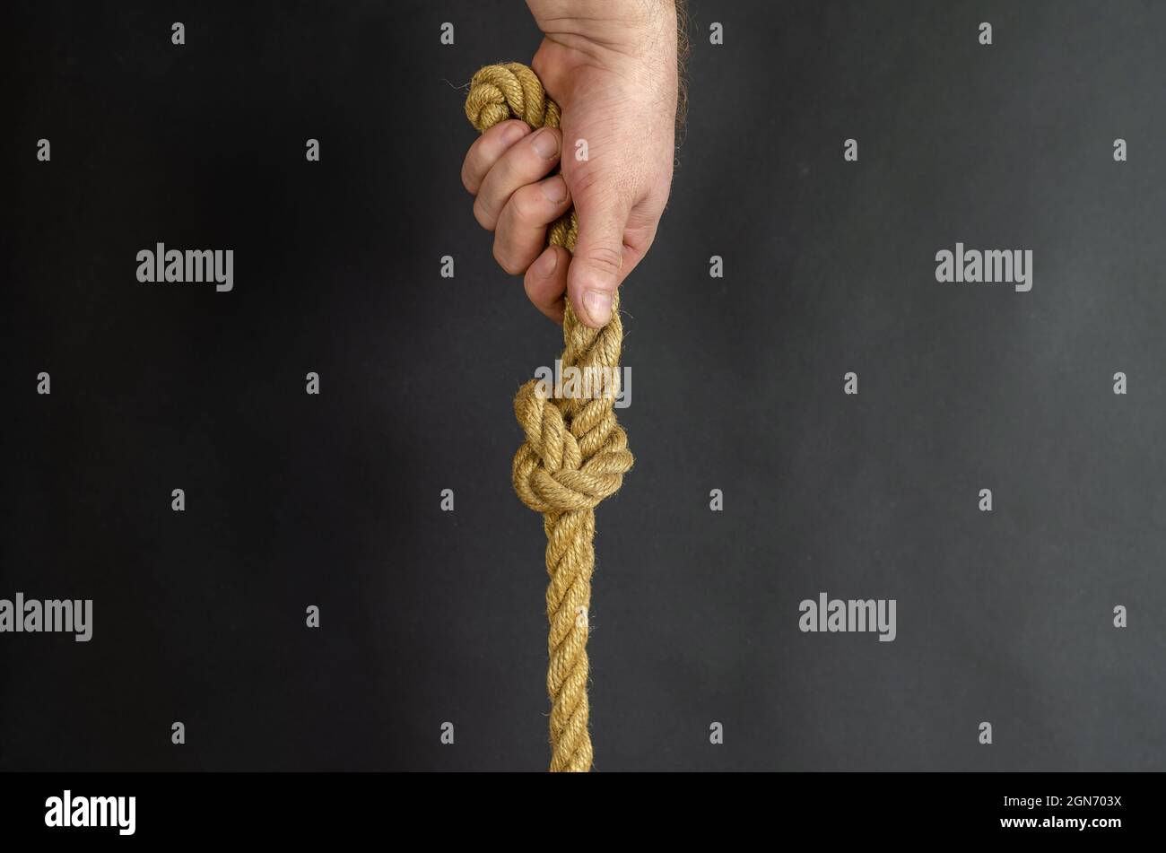 Adult Male holds vertically a rope with a knot. Hand holds a yel Stock