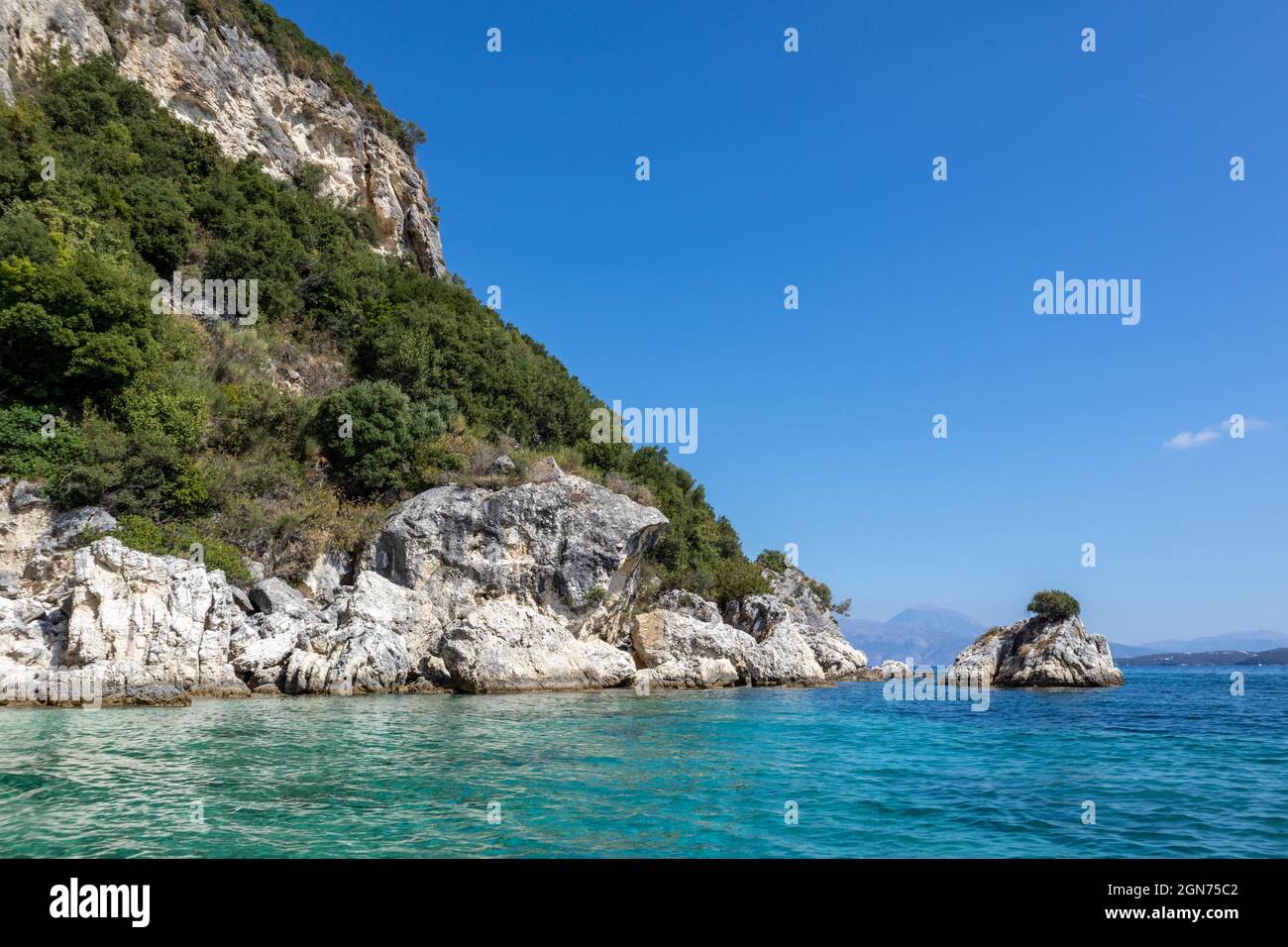 Turquoise Ionian Sea with scenic green cliffs, rocks in water and bright sky. Nature of Ormos Desimi, Lefkada island in Greece. Summer vacation idylli Stock Photo