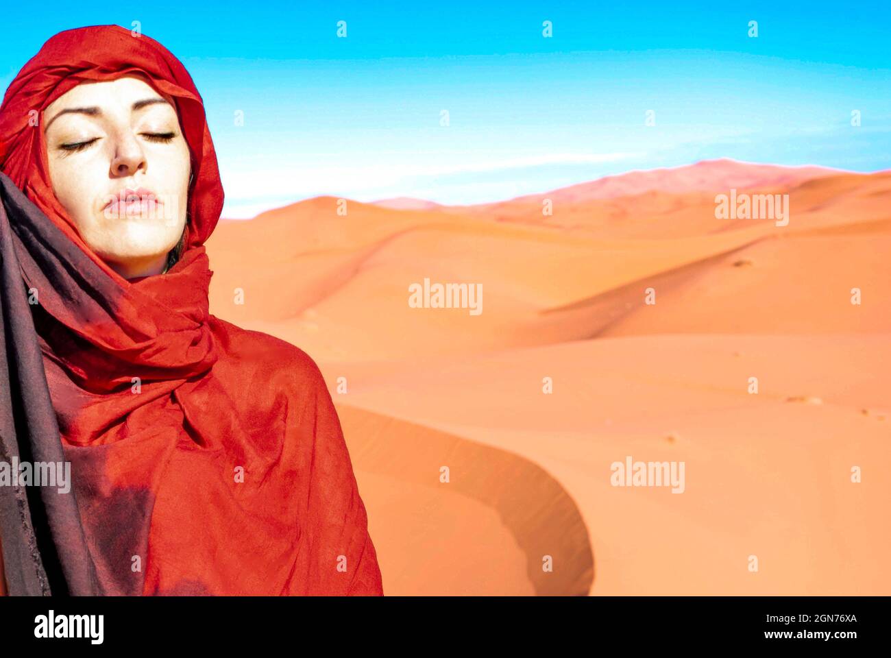 Portrait of a Caucasian woman meditating with a red headscarf in the desert sun Stock Photo