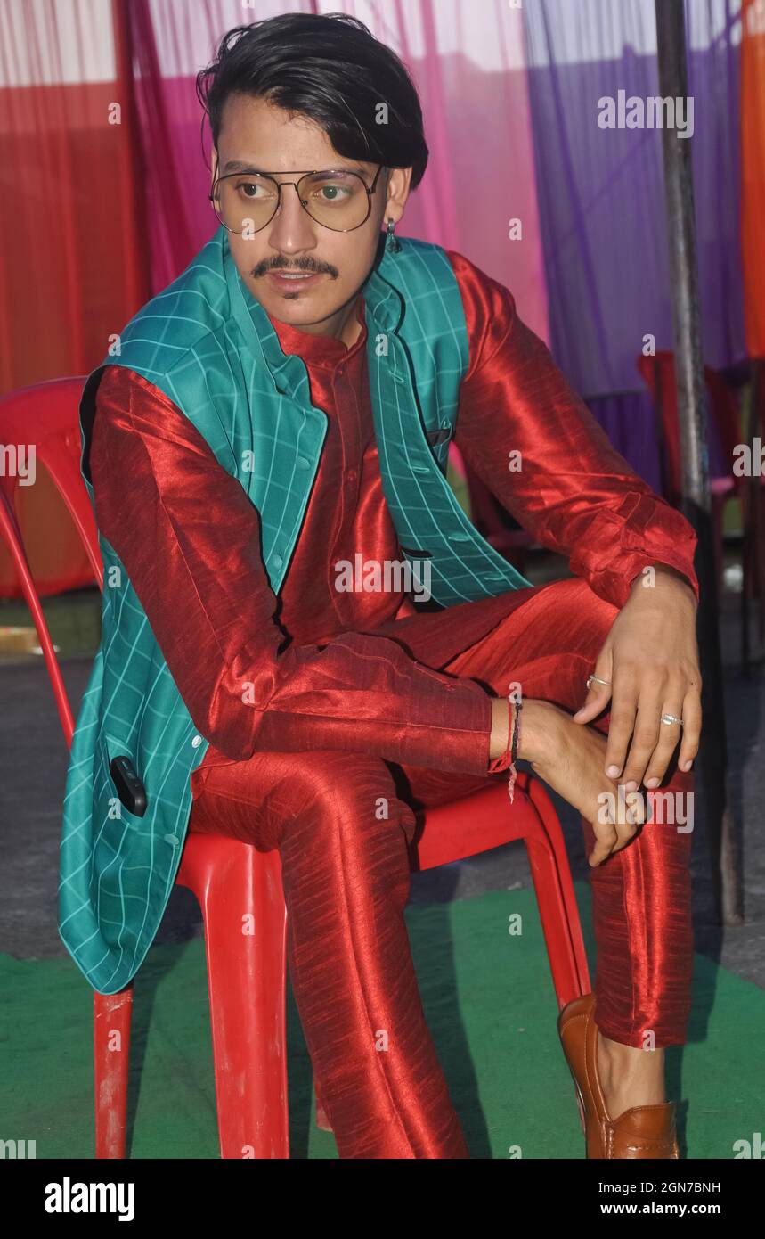 A good looking Indian young guy posing with sitting on chair with wearing kurta, pajama, nehru coat and sunglasses with looking sideways Stock Photo