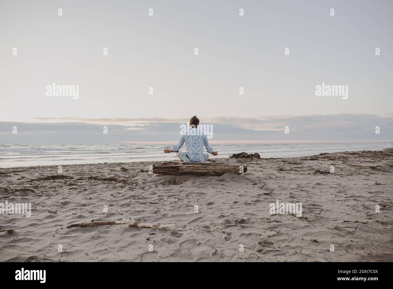 Caucasian boy practicing yoga by the sea at sunrise - Man practicing yoga pose to meditation on the beach at sunset - Healthy with yoga concept Stock Photo
