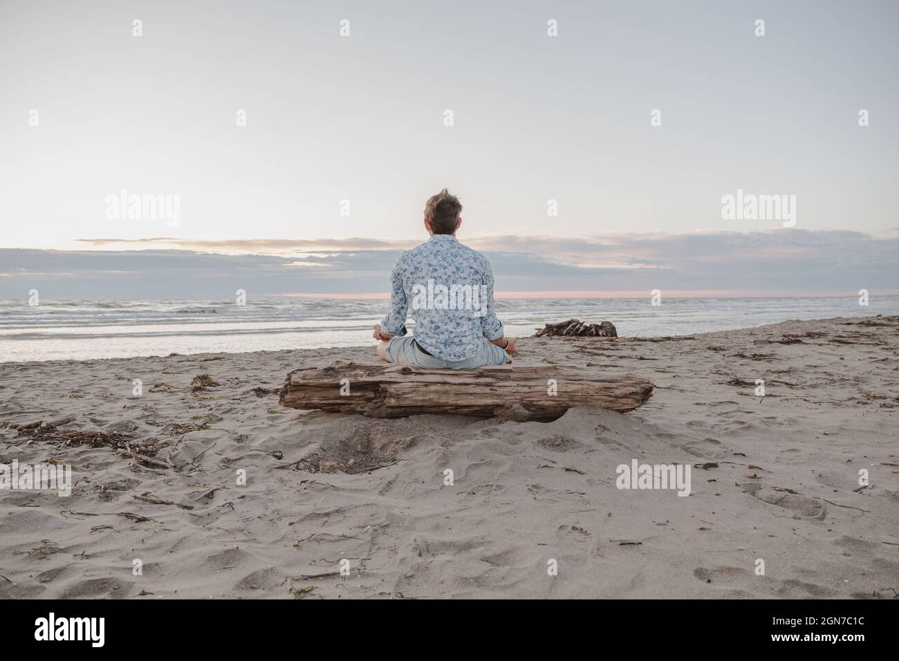 Caucasian boy practicing yoga by the sea at sunrise - Man practicing yoga pose to meditation on the beach at sunset - Healthy with yoga concept Stock Photo