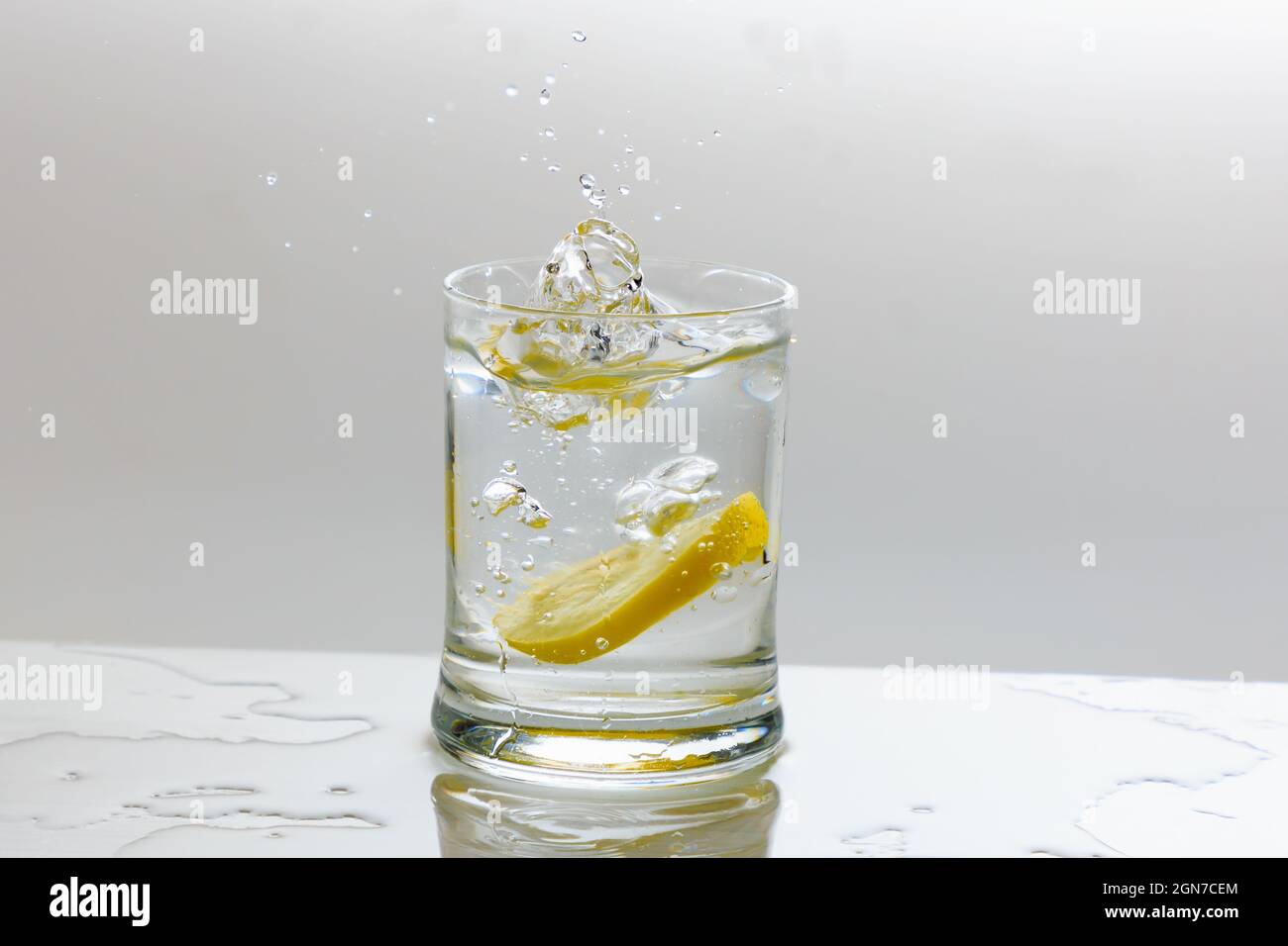 Slice on lemon splashing into a glass tumbler filled with water Stock