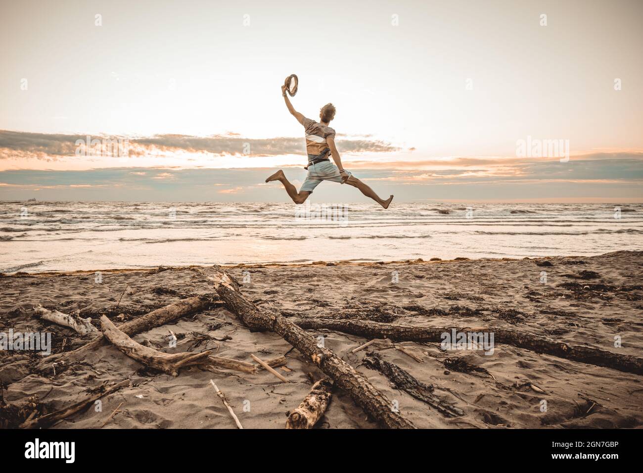 Happy boy enjoying summer holidays on beach at sunset - Young man jumping on the beach at the sunrise - Vacations concept Stock Photo