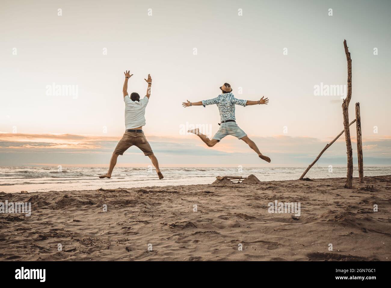 Happy friends enjoying summer holidays on beach at sunset - Two boys jumping on the beach at the sunrise - Vacations concept Stock Photo