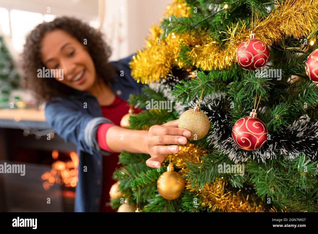 Happy african american woman hanging baubles on christmas tree Stock Photo