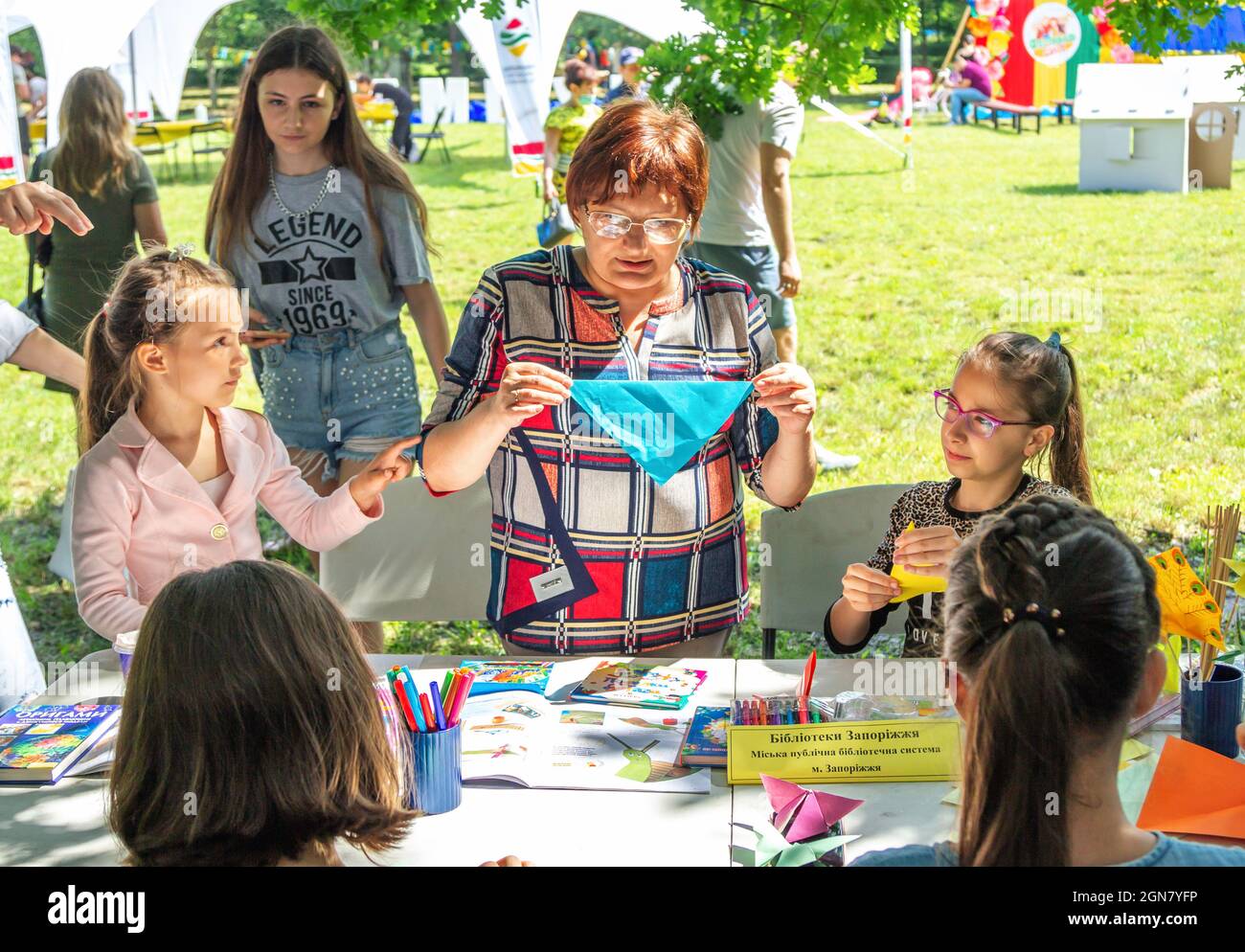 Zaporizhia, Ukraine- June 19, 2021: Charity Family festival:  woman – volunteer entertaining children, making origami at art and craft outdoors worksh Stock Photo