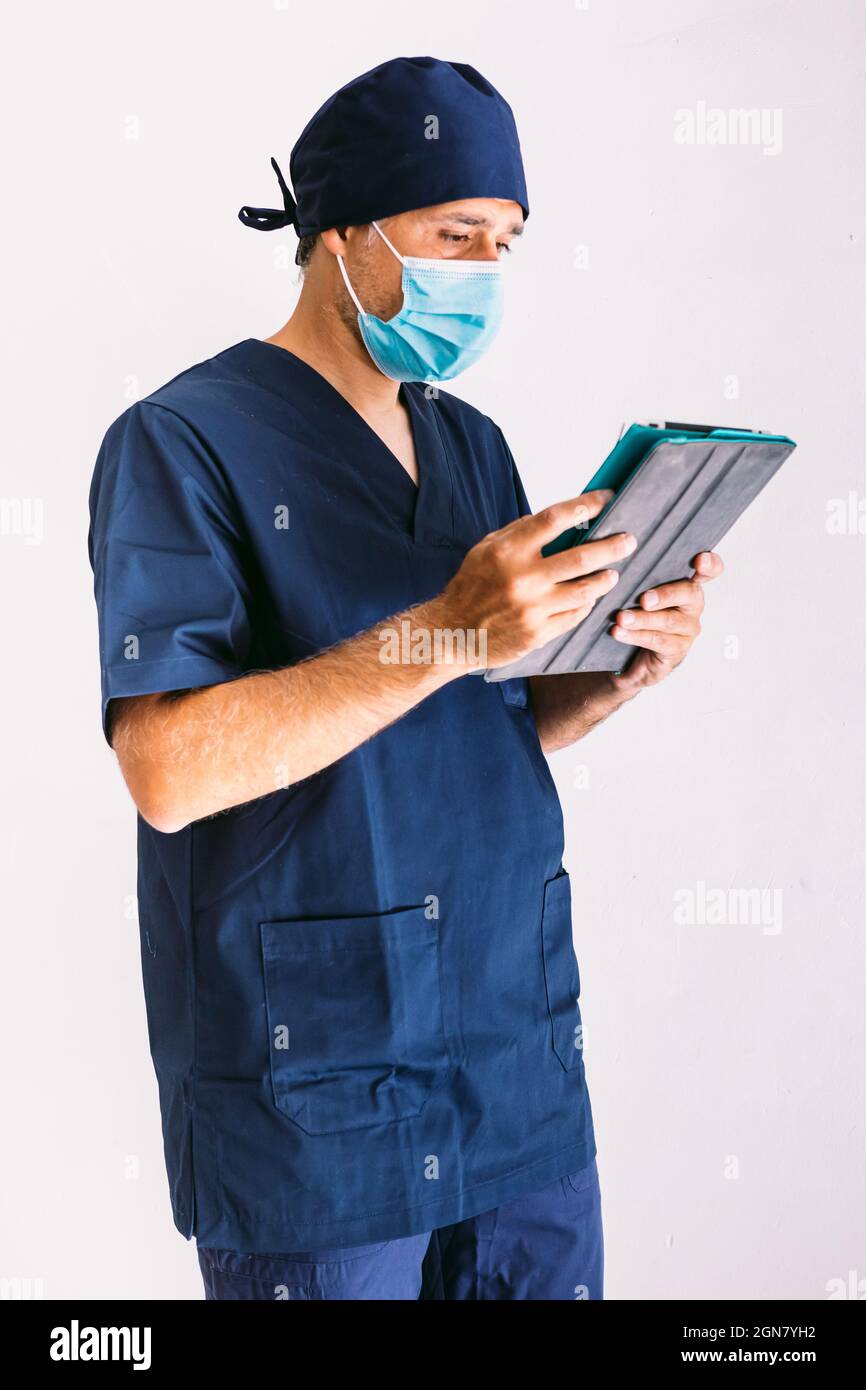 Male nurse, doctor or vet in blue uniform at a window in a hospital, looking at a tablet. Medicine, hospital and healthcare concept. Stock Photo