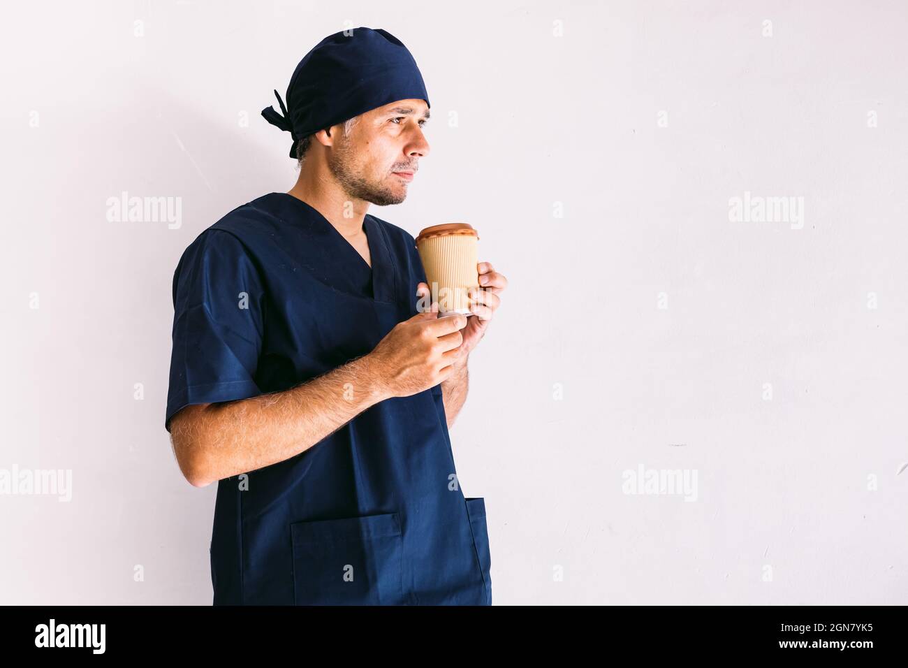 Male nurse, doctor or vet in dark blue uniform looking out of a window in a hospital, having coffee: Medicine, hospital and healthcare concept. Stock Photo