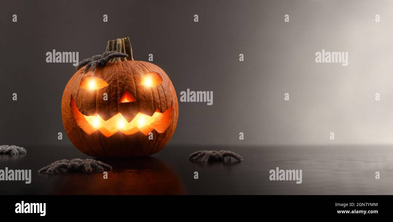 Greeting card for halloween with carved and illuminated pumpkin with spiders and dark isolated background. Front view. Horizontal composition. Stock Photo