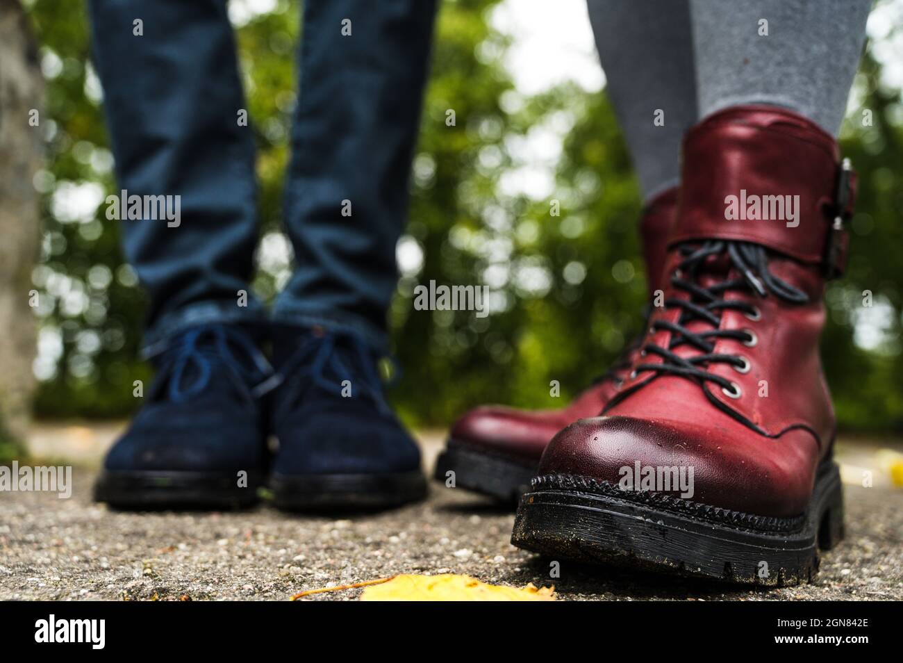 Burgundy leather boots. Blue suede shoes. Boy and girl. Asphalt with fallen leaves. Autumn fashion footwear. Stock Photo
