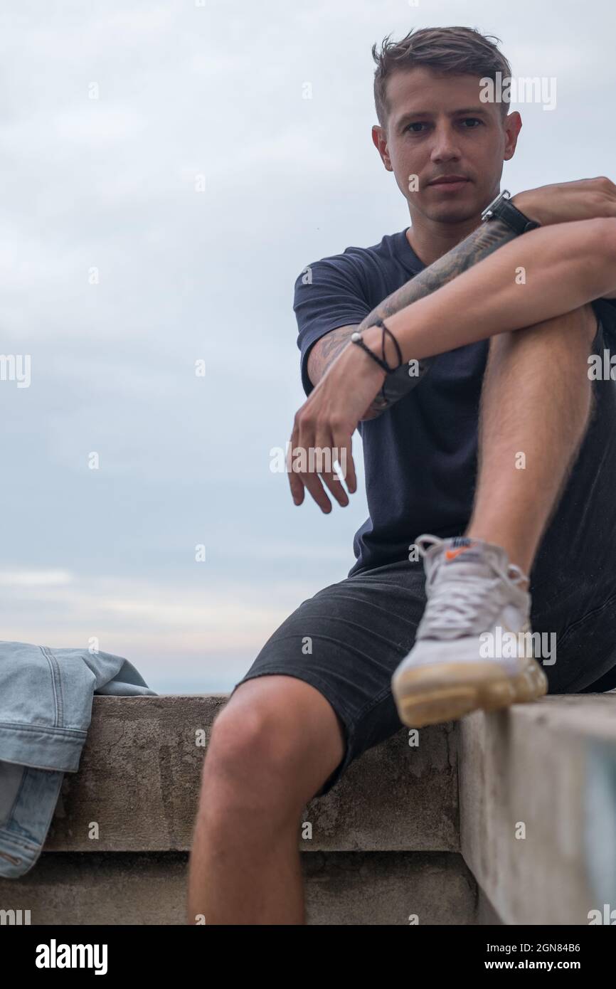 Portrait of young handsome pretty Caucasian man in casual wearing and sneakers. Sitting and looking at camera with copy space Stock Photo
