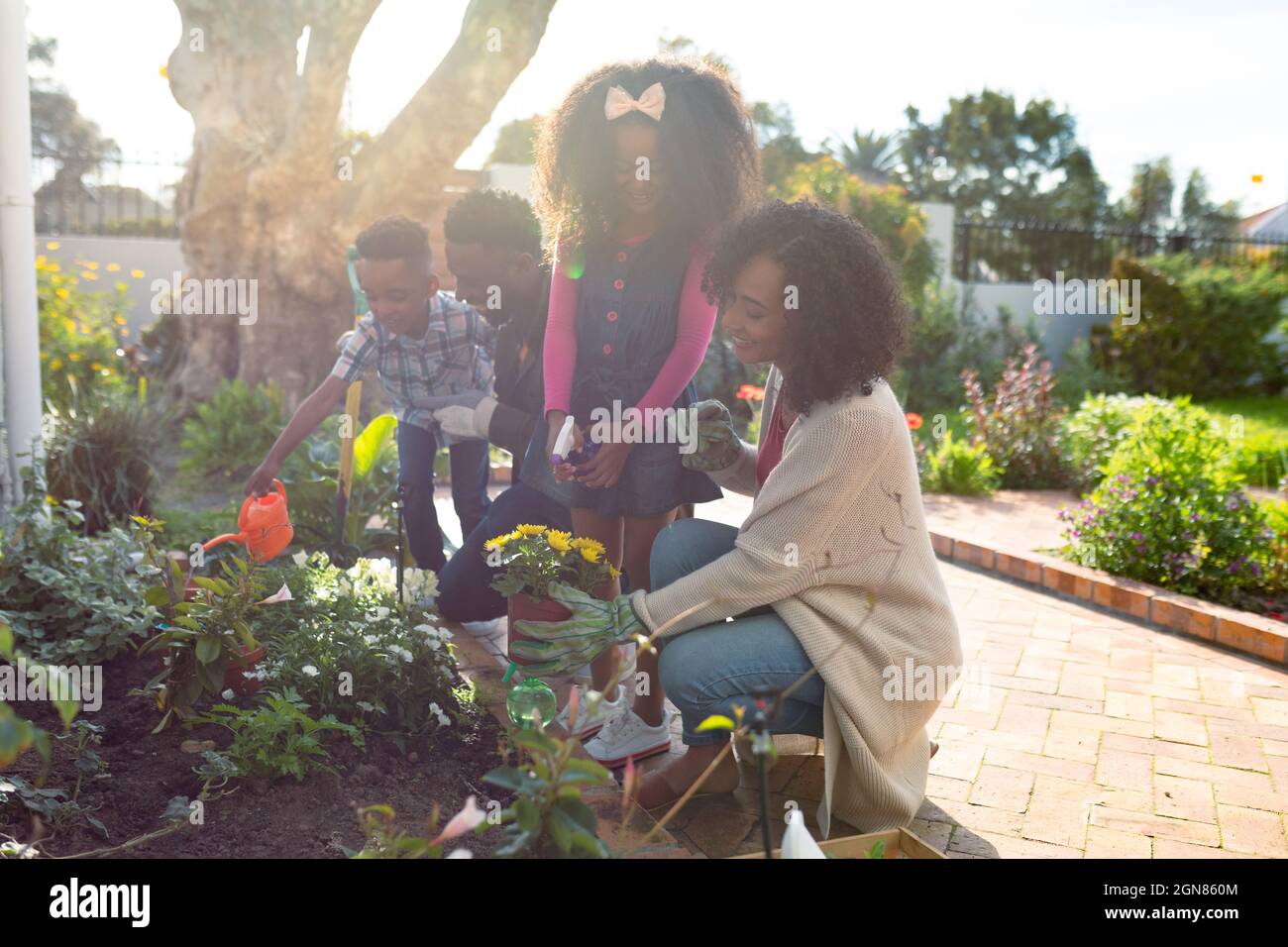 Happy african american family planting flowers and watering plants ...