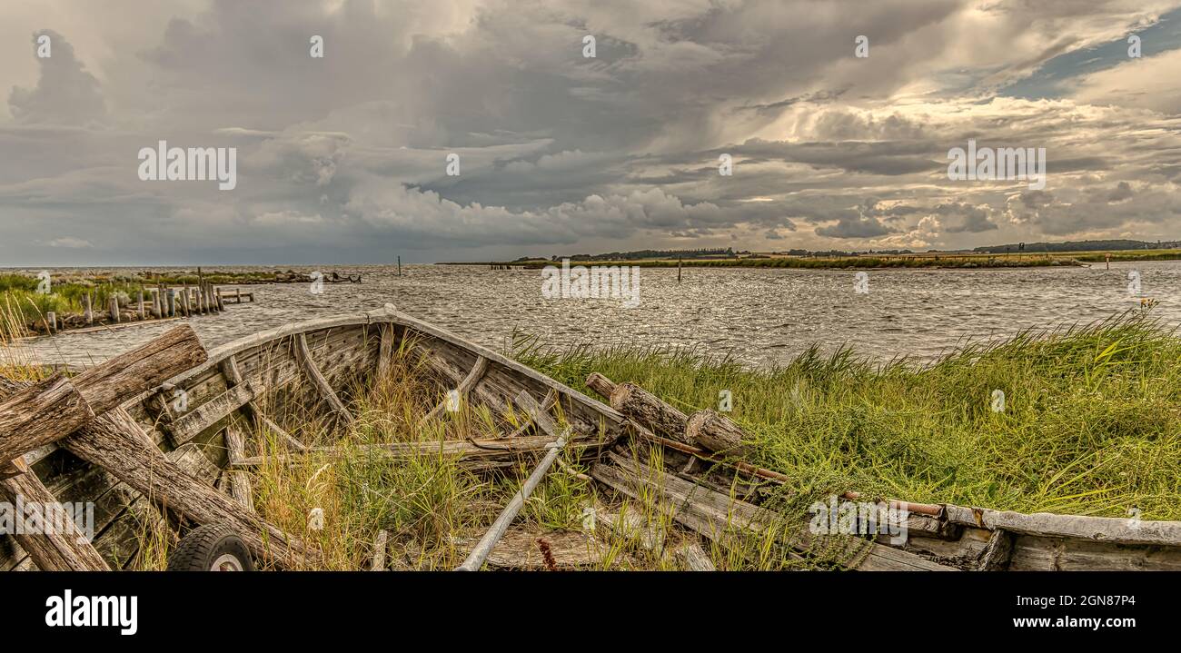 a wrecked wooden boat on the shore with grass growing over the railing, Bisserup, Denmark, August 8, 2021 Stock Photo