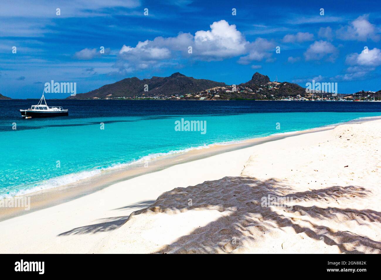 Caribbean Beach with Palm Tree Shadow, Turquoise Caribbean ocean, Moored Boat and Union island:  Casuarina Beach, Palm Island, SVG. Stock Photo