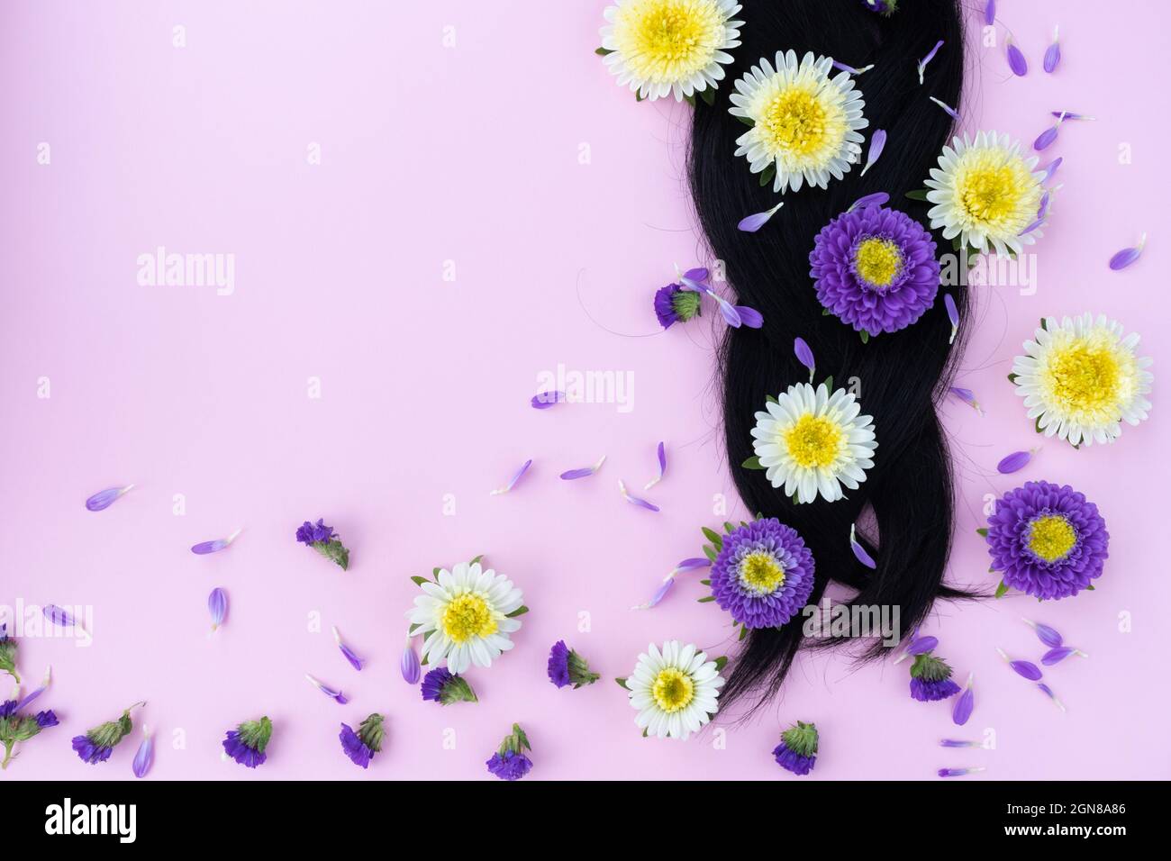 Pigtail from dark hair with fresh flowers in it. Hair care concept. Stock Photo