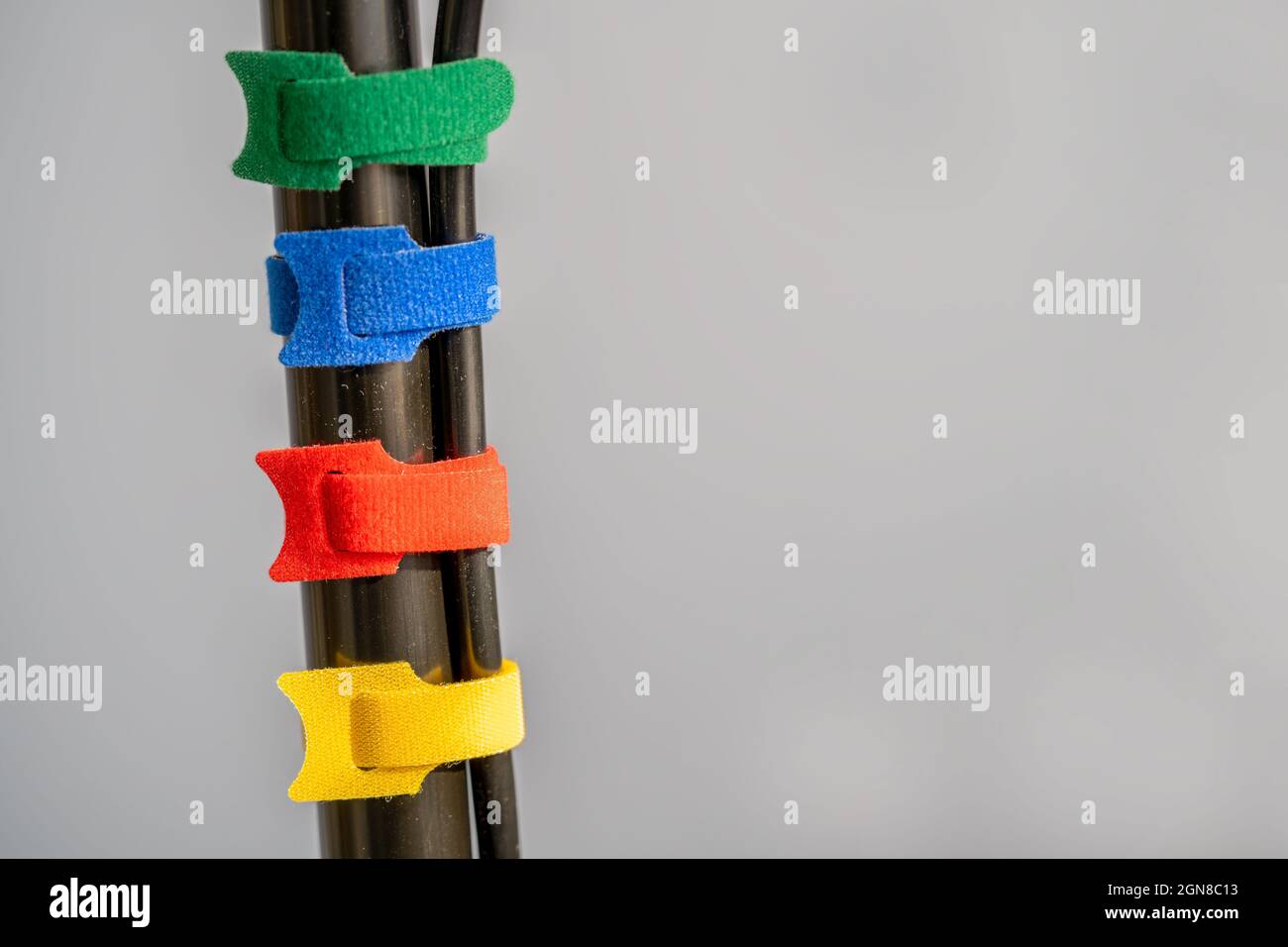 four multicolored hook and loop fabric cable ties connecting power cables together on a plain grey background Stock Photo