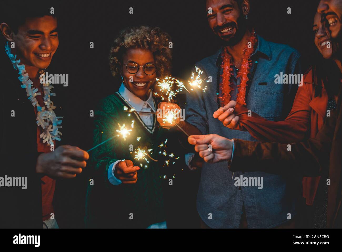 Happy diverse friends celebrating with sparklers on new year eve - Soft focus on african woman face Stock Photo
