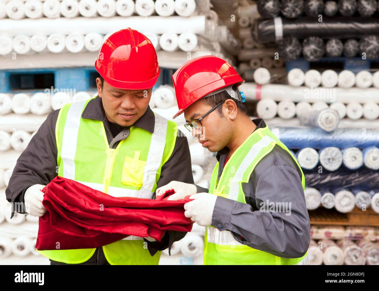Two textile factory workers checking raw material fabric colour red in warehouse Stock Photo Alamy