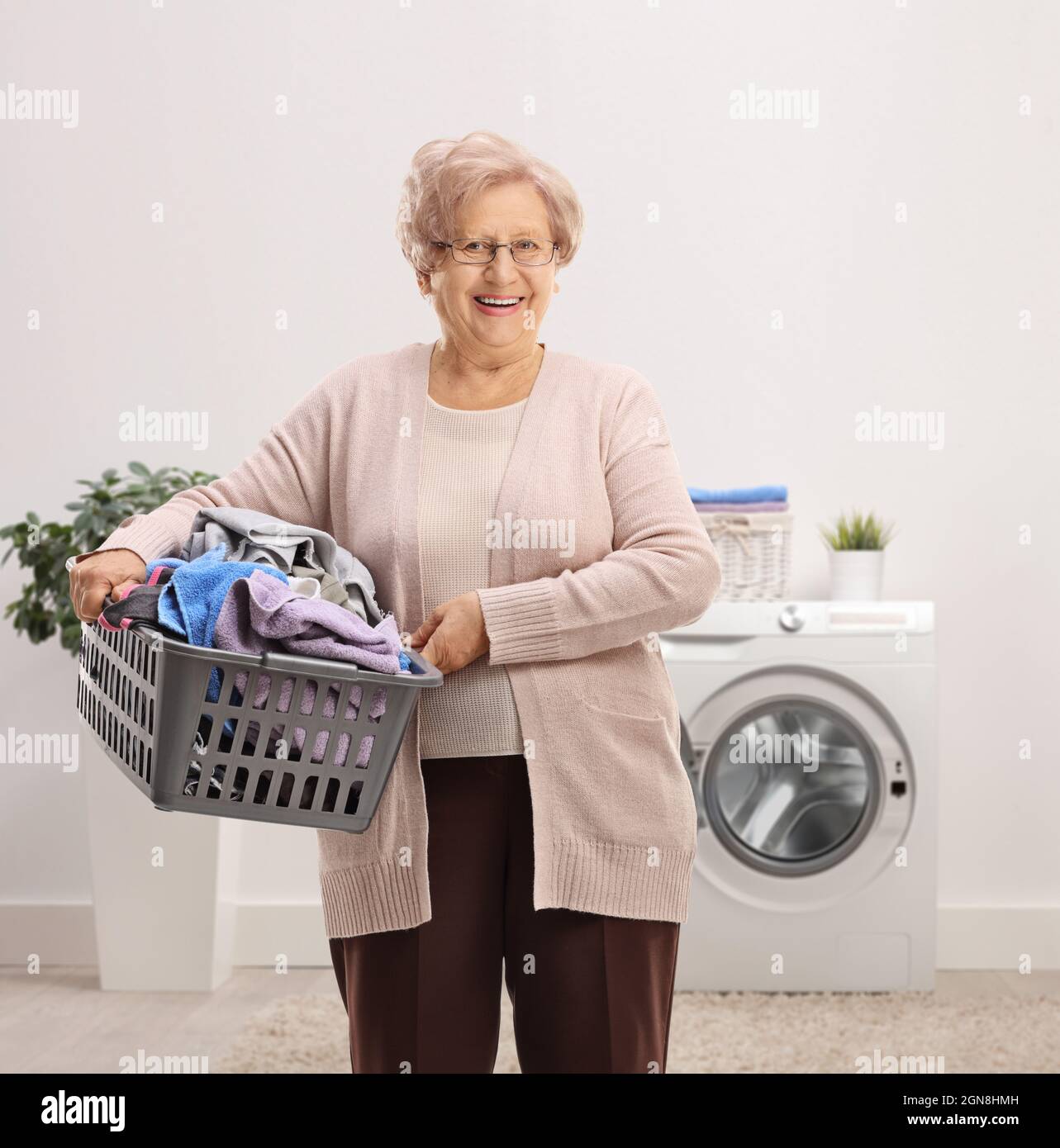 Elderly woman holding a laundry basket with clothes inside a bathroom Stock Photo