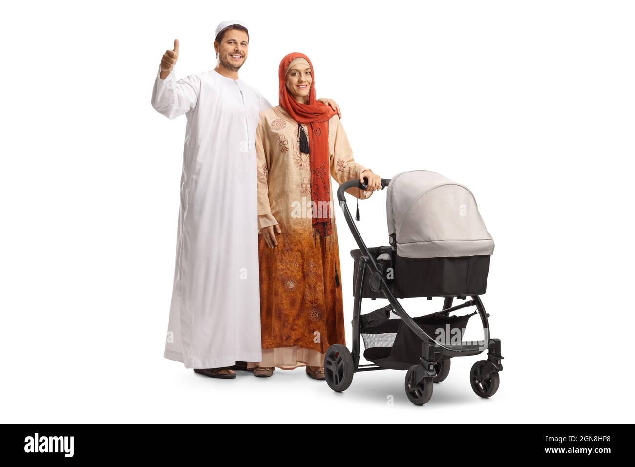 Full length portrait of a man and woman in ethnic clothes posing with a pushchair and gesturing thumbs up isolated on white background Stock Photo