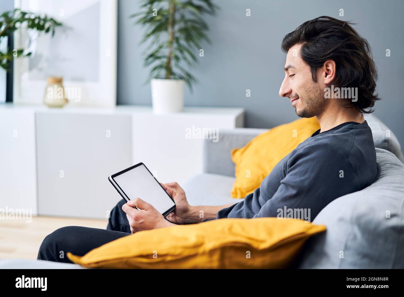 Man using digital tablet while sitting on sofa Stock Photo