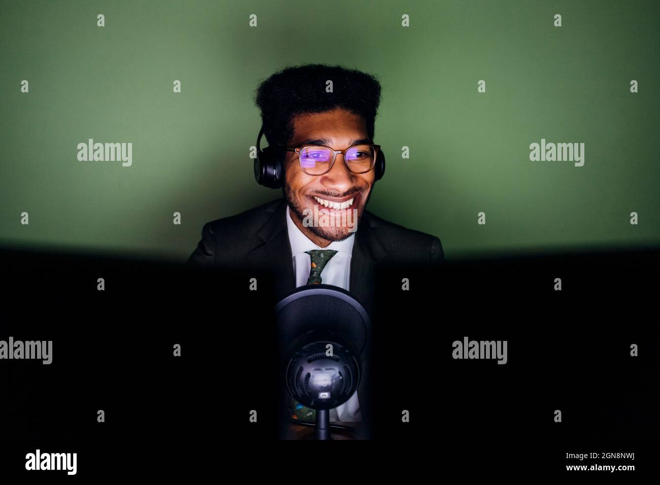 Smiling male professional with headphones live streaming at home Stock Photo