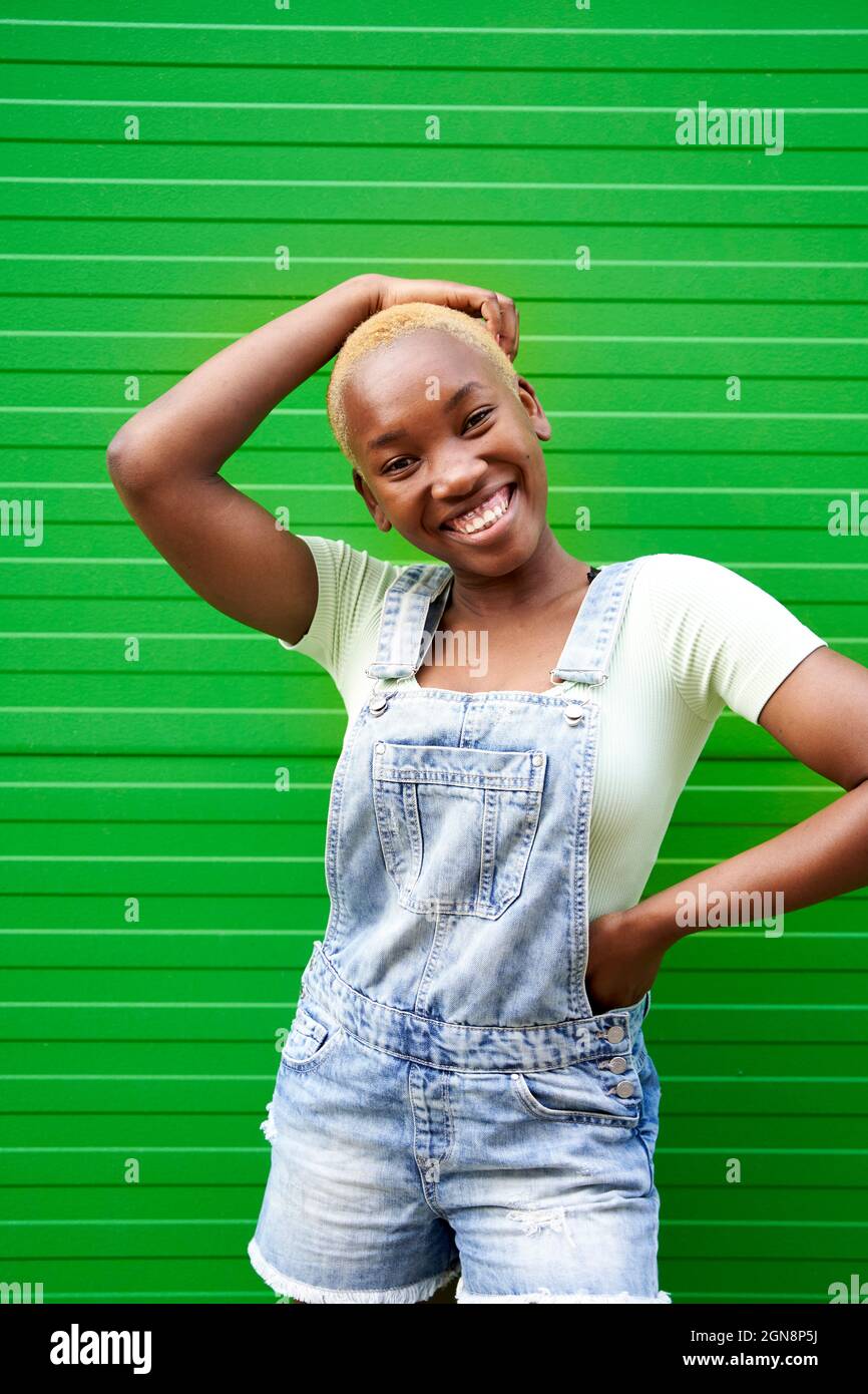 Happy young woman standing with hand on hip in front of green wall
