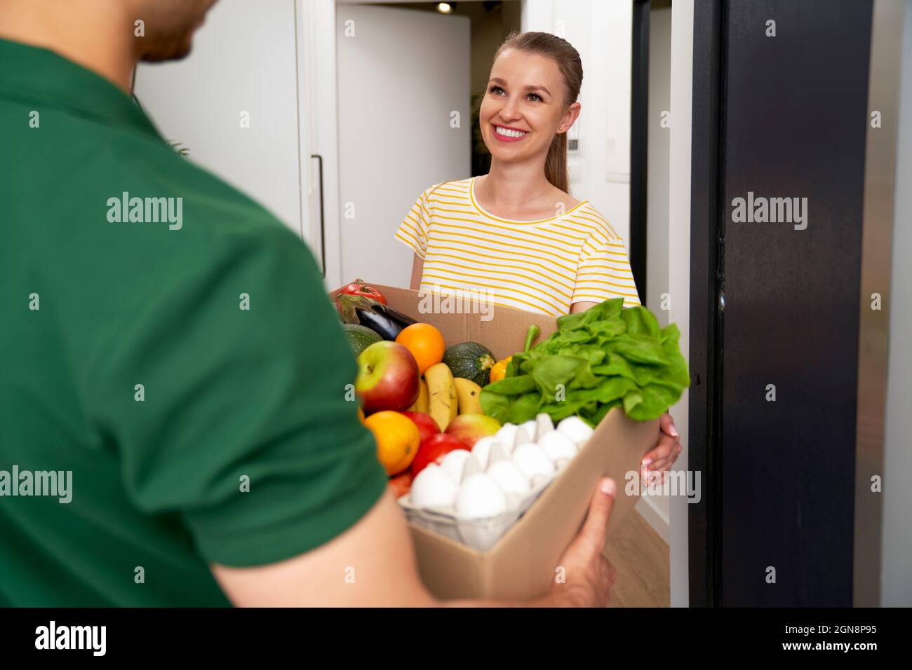 Smiling woman receiving groceries from delivery person at entrance Stock Photo