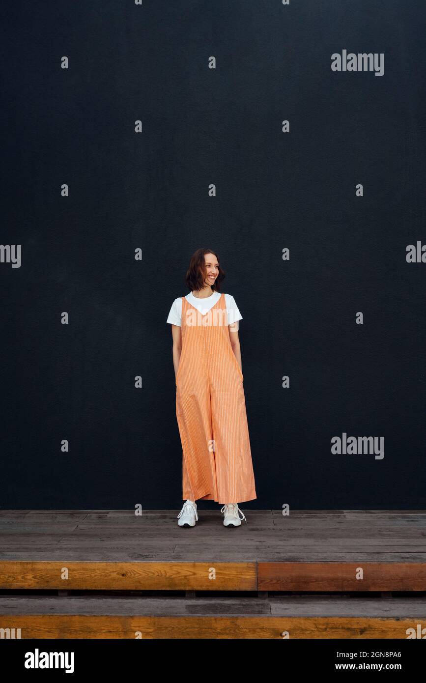 Smiling woman with hands in pockets standing in front of wall Stock ...