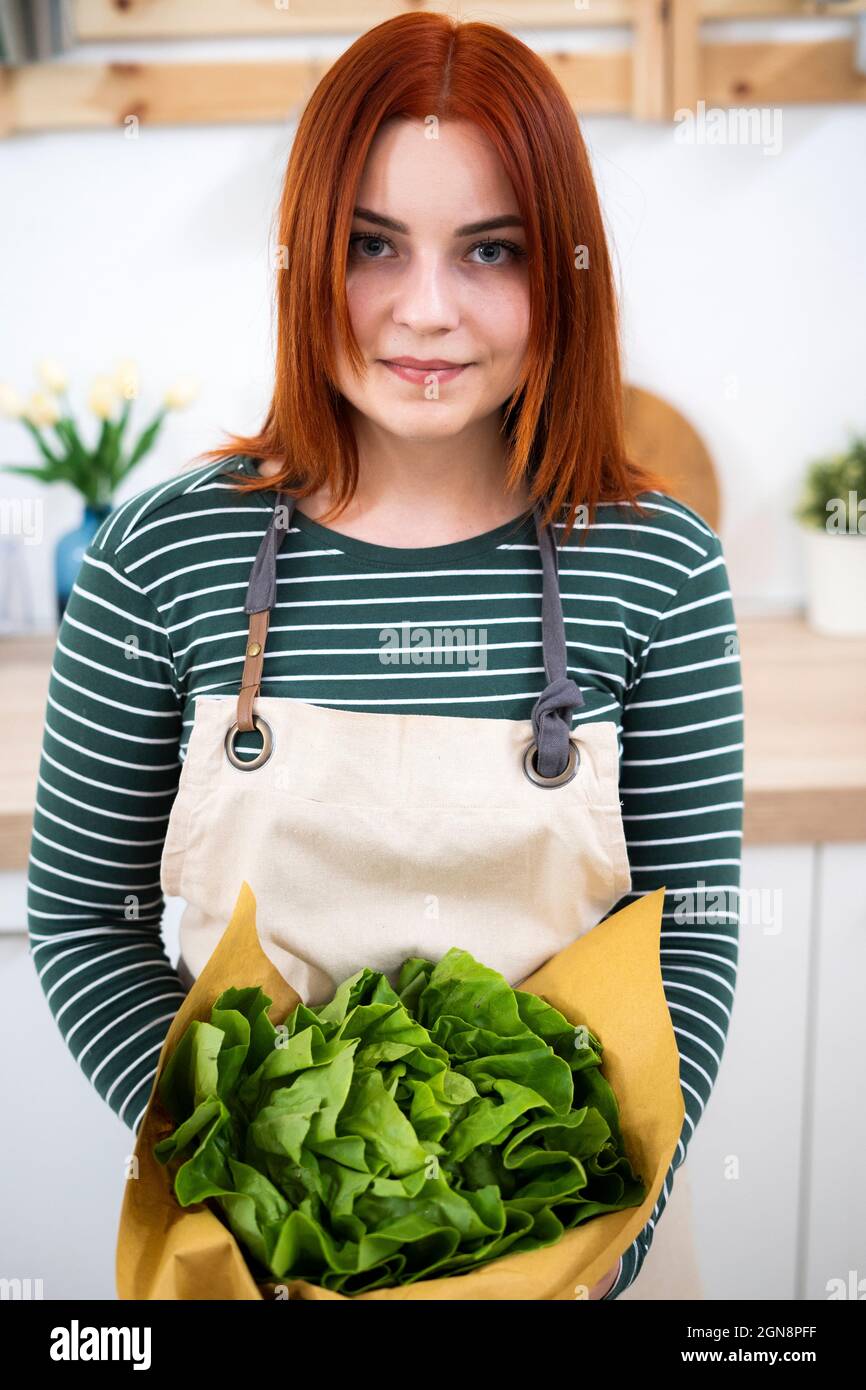 Woman with apron holding leaf vegetable in kitchen Stock Photo
