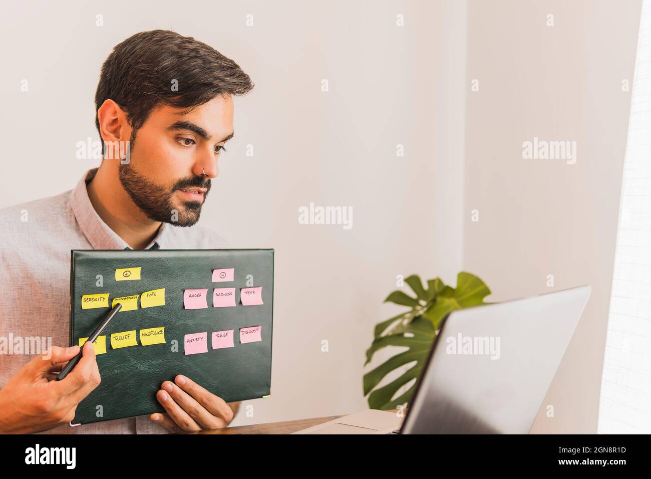 Young male psychologist explaining emotions chart during video call through laptop at office Stock Photo