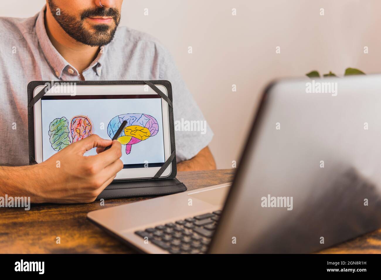Male mental health professional showing brain diagram on digital tablet during online therapy Stock Photo
