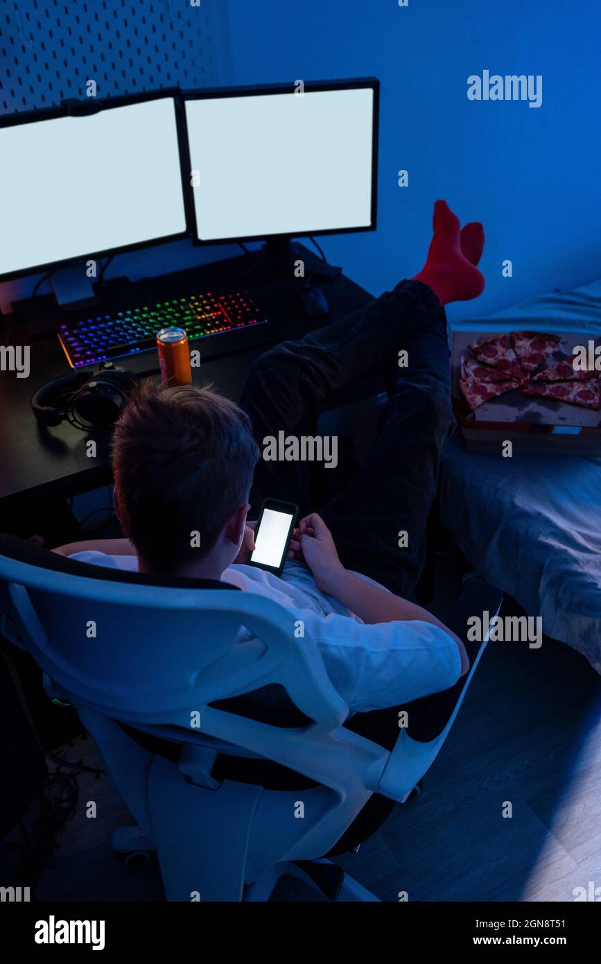 Boy using smart phone while sitting on chair by computer table Stock Photo