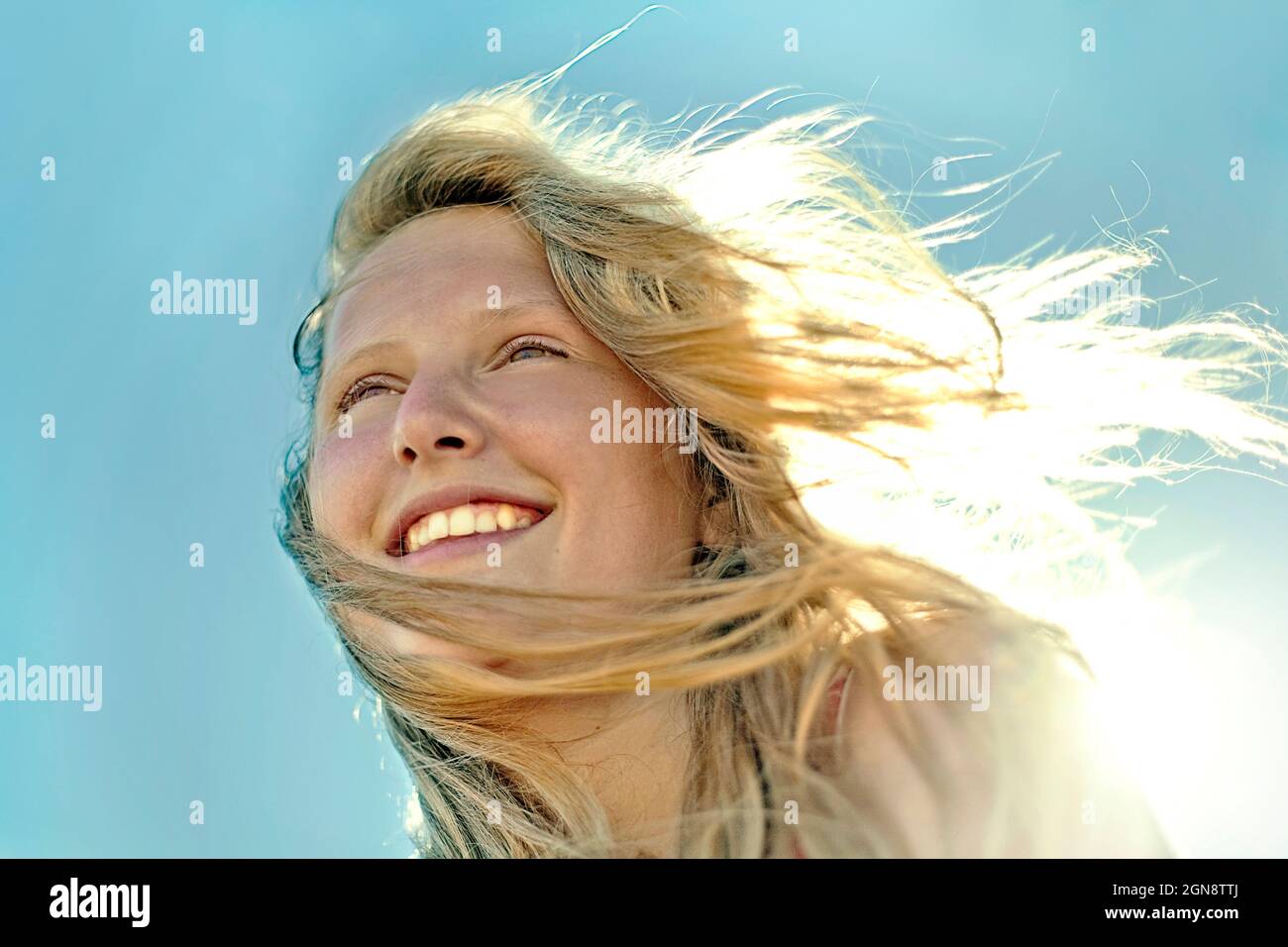 Smiling pre-adolescent girl with blond hair in front of clear sky Stock Photo