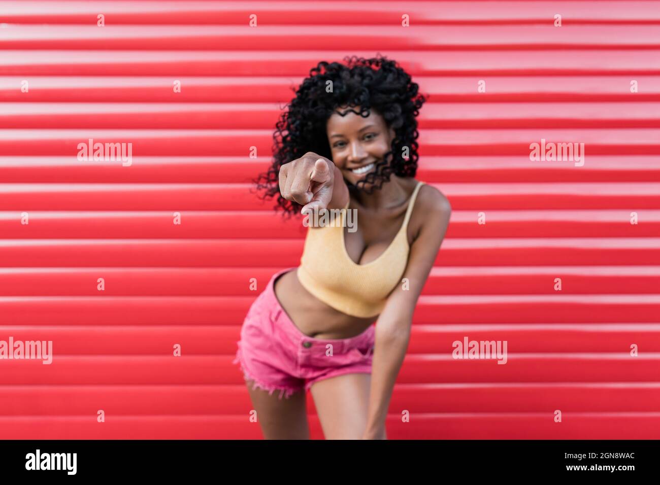 Smiling young woman pointing while standing in front of red shutter Stock Photo