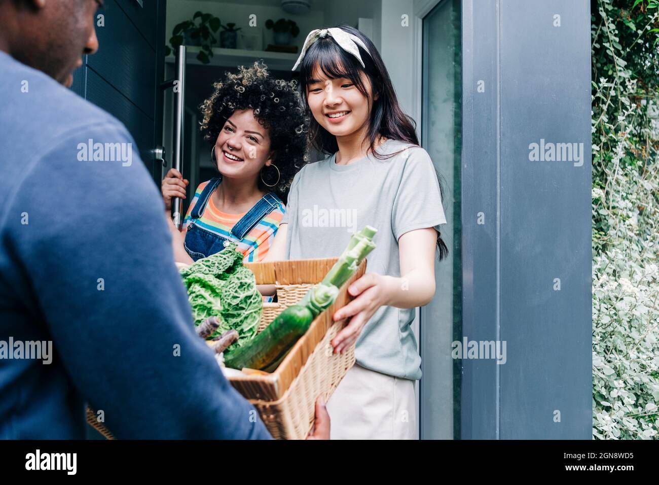Male delivery person delivering fresh vegetable to women at doorway Stock Photo