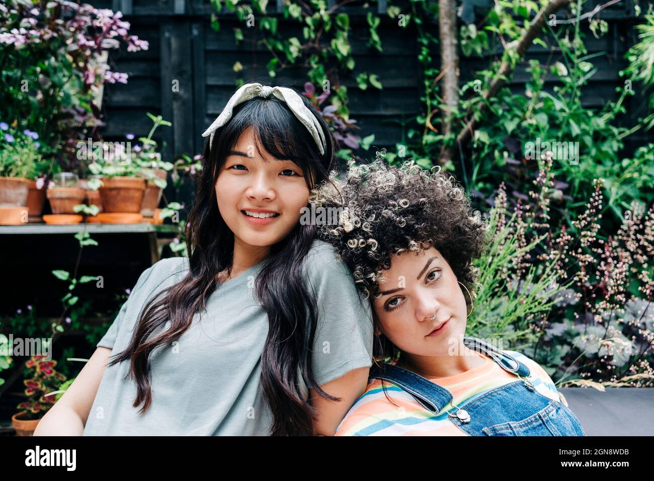 Smiling friends leaning on each other while resting at backyard Stock