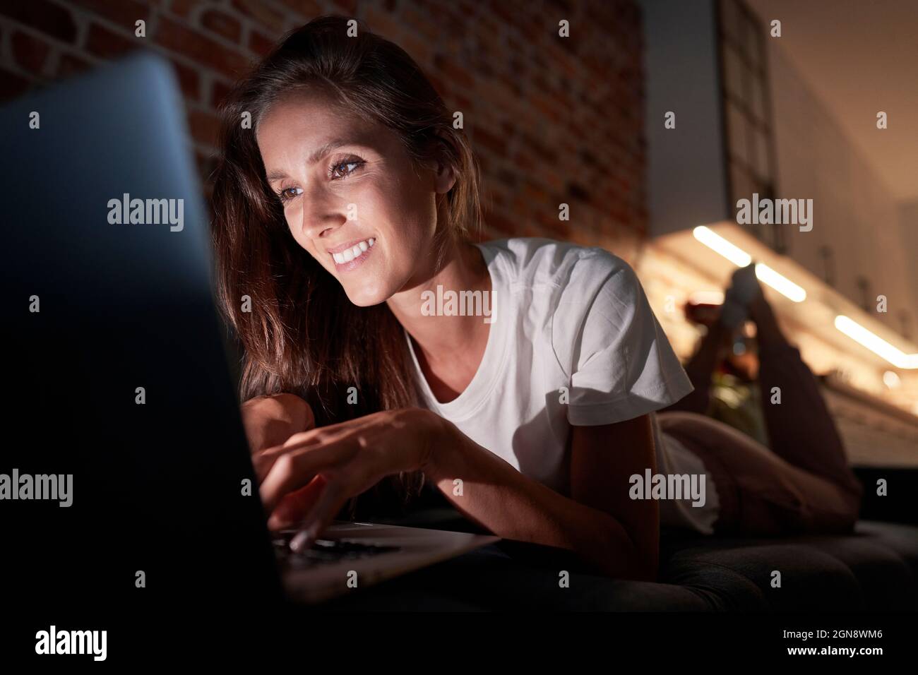 Young woman using laptop while lying on sofa at home during night Stock ...