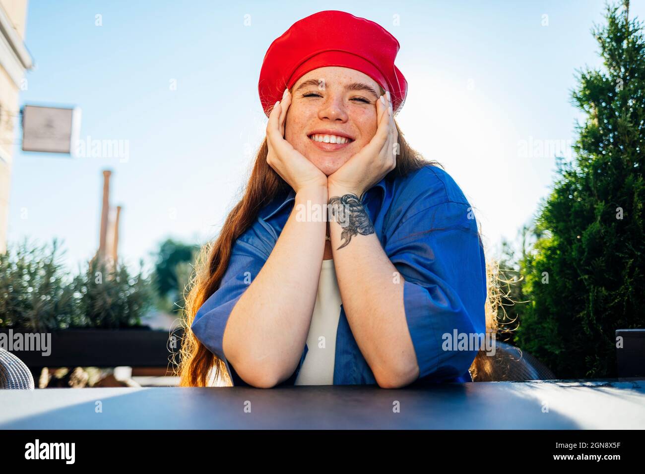 Smiling young woman with hands on chin sitting in cafe Stock Photo - Alamy